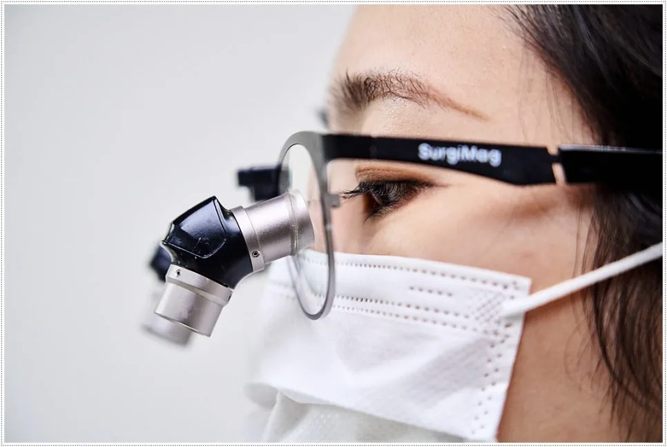 Close-up side profile of a masked clinician wearing SurgiMag dental magnifying loupes.