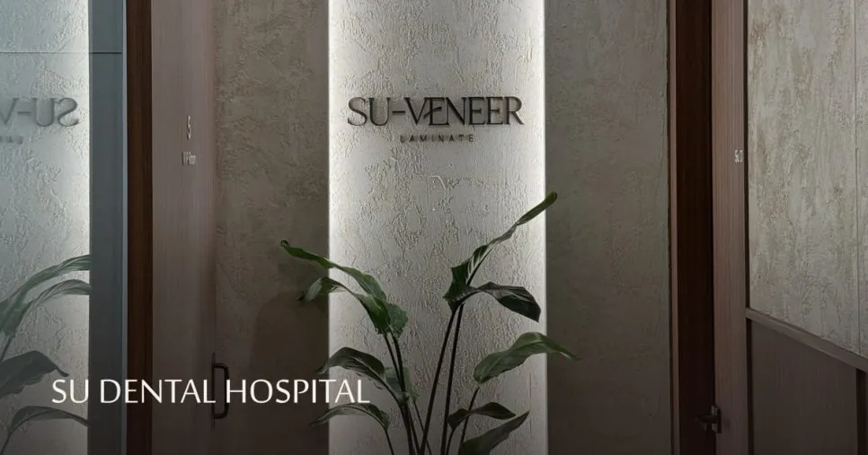 The entrance wall of SU Dental Hospital displaying the SU-VENEER logo beside a green plant.
